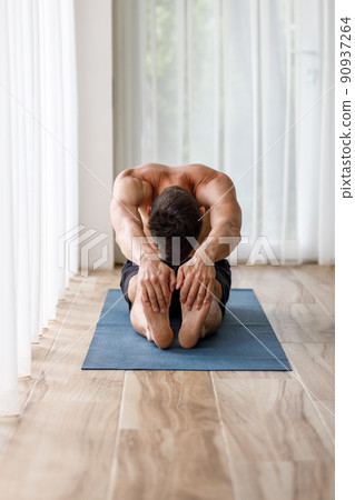 Young yoga man doing stretching legs during morning routine Young yoga man doing stretching legs during morning routine 90937264