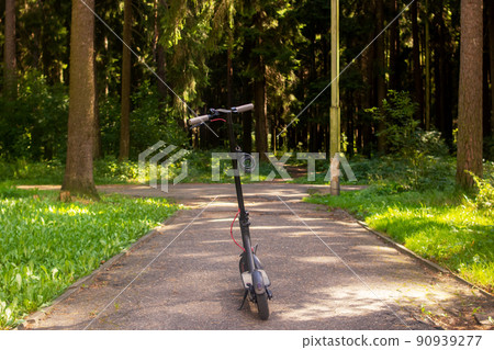 Electric scooter on a green forest background Electric scooter on a green forest background 90939277