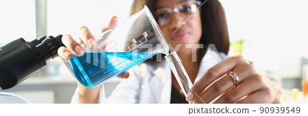Dark-skinned woman scientist pouring blue liquid 90939549