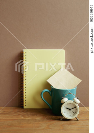Notebook and mug cup and alarm clock on wooden desk. brown wall background. workspace Notebook and mug cup and alarm clock on wooden desk. brown wall background. workspace 90939945