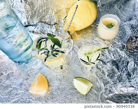 Cold lemon drink into which one can add some alcohol with ice cubes and mint on steel background with candles Cold lemon drink into which one can add some alcohol with ice cubes and mint on steel background with candles 90940336
