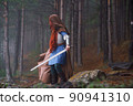 Red-haired girl in armor and raincoat in forest. Historical concept 90941310