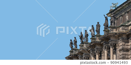 Old roof statutes of high ranked priests and saints lined up in Catholic Cathedral of Holy Trinity, Hofkirche in downtown of Dresden, Germany, details, at blue sky solid background with copy space. 90941493