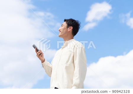 一個年輕人手裡拿著智能手機，仰望天空 90942328