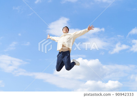 A young man jumping with his arms open under the blue sky A young man jumping with his arms open under the blue sky 90942333