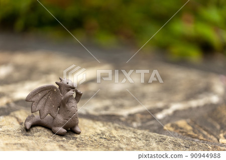 A cute unglazed dragon figurine placed on a stone pavement 90944988