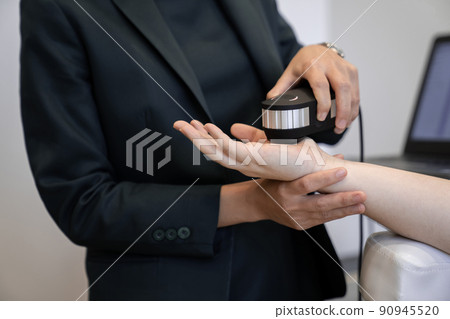 Woman doctor in a dark uniform suit is testing a patient's hand for her health statistic that show on the laptop monitor 90945520