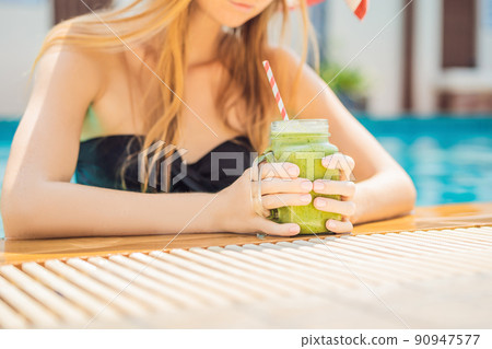 Woman with a green smoothies of spinach and banana on the background of the pool. Healthy food, healthy smoothies Woman with a green smoothies of spinach and banana on the background of the pool. Healthy food, healthy smoothies 90947577