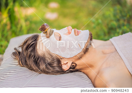 Young man makes a face mask with snail mucus. Snail crawling on a face mask. SPA for man, SPA for all Young man makes a face mask with snail mucus. Snail crawling on a face mask. SPA for man, SPA for all 90948243