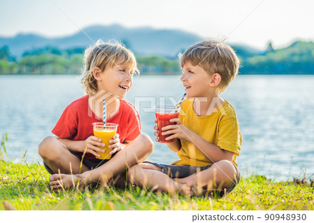 Two boys drink healthy smoothies against the backdrop of palm trees. Mango and watermelon smoothies. Healthy nutrition and vitamins for children Two boys drink healthy smoothies against the backdrop of palm trees. Mango and watermelon smoothies. Healthy nutrition and vitamins for children 90948930