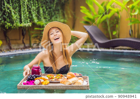 Breakfast tray in swimming pool, floating breakfast in luxury hotel. Girl relaxing in the pool drinking smoothies and eating fruit plate, smoothie bowl by the hotel pool. Exotic summer diet. Tropical Breakfast tray in swimming pool, floating breakfast in luxury hotel. Girl relaxing in the pool drinking smoothies and eating fruit plate, smoothie bowl by the hotel pool. Exotic summer diet. Tropical 90948941