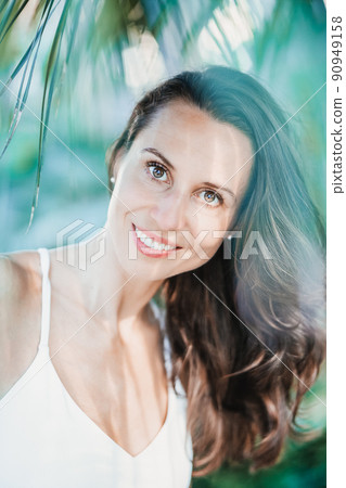 Young beautiful natural cheerful woman with healthy face and skin in exotic greenery. Closeup fresh face of attractive girl. Summer model. Natural beauty concept Young beautiful natural cheerful woman with healthy face and skin in exotic greenery. Closeup fresh face of attractive girl. Summer model. Natural beauty concept 90949158