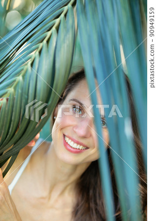 Young beautiful natural cheerful woman with healthy face and skin in exotic greenery. Closeup fresh face of attractive girl. Summer model. Natural beauty concept Young beautiful natural cheerful woman with healthy face and skin in exotic greenery. Closeup fresh face of attractive girl. Summer model. Natural beauty concept 90949159