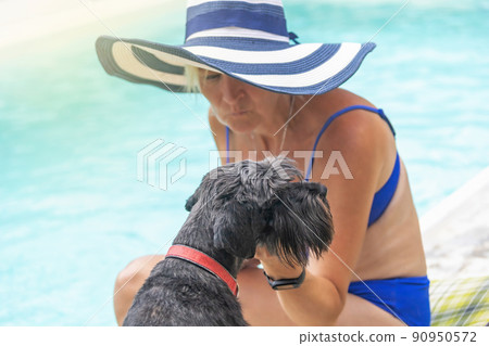 Woman wearing summer straw hat is posing with black schnauzer dog closeup. Woman wearing summer straw hat is posing with black schnauzer dog closeup. 90950572