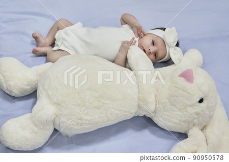 White dreesed newborn baby with her white bunny toy. Cute mixed race baby girl looking into the camera 90950578