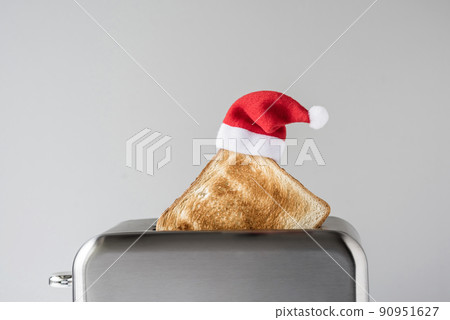 Roasted toast bread in a christmas Santa Claus red hat popping up of stainless steel retro toaster for breakfast preparation. Concept 90951627