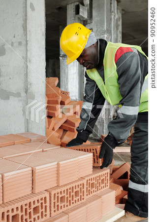 Mature experienced black man in workwear bending over stack of bricks 90952460