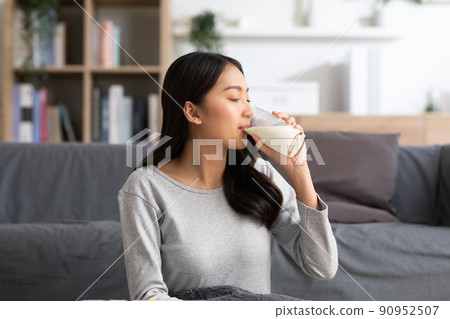 Healthy Young Asian woman Drinking milk with calcium for strong bone at home. Smiling indian woman holding soy milk on glass enjoy with nutrition wellness life.Wellness with natural milk fresh Concept 90952507