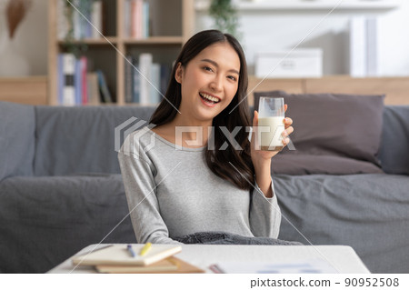 Healthy Young Asian woman Drinking milk with calcium for strong bone at home. Smiling indian woman holding soy milk on glass enjoy with nutrition wellness life.Wellness with natural milk fresh Concept 90952508