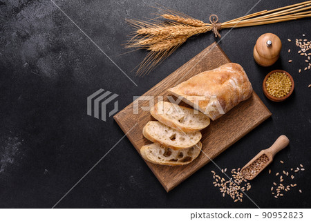 French baguette bread sliced on a wooden cutting board against a dark concrete background 90952823