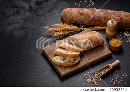 French baguette bread sliced on a wooden cutting board against a dark concrete background French baguette bread sliced on a wooden cutting board against a dark concrete background 90952824