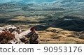 A male traveler is sitting on the edge of a cliff. A male traveler is sitting on a rock with a bird's-eye view of the valley. The concept of recreation and tourism. The man enjoys the beautiful views 90953176