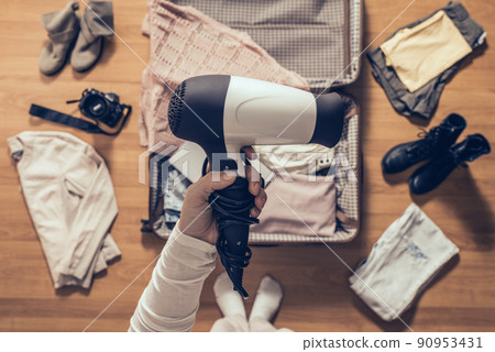 Top view on the woman holds hair dryer packing clothes in the open suitcase. Travel concep Top view on the woman holds hair dryer packing clothes in the open suitcase. Travel concep 90953431