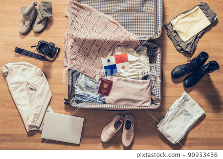Woman's clothes, laptop, camera, russian passport and flag of Panama lying on the parquet floor near and in the open suitcase. Travel concept Woman's clothes, laptop, camera, russian passport and flag of Panama lying on the parquet floor near and in the open suitcase. Travel concept 90953436