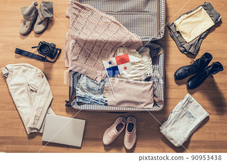 Woman's clothes, laptop, camera, russian passport and flag of Panama lying on the parquet floor near and in the open suitcase. Travel concept 90953438