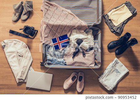 Woman's clothes, laptop, camera and flag of Iceland lying on the parquet floor near and in the open suitcase. Travel concept Woman's clothes, laptop, camera and flag of Iceland lying on the parquet floor near and in the open suitcase. Travel concept 90953452