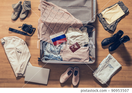 Woman's clothes, laptop, camera, russian pasport and flag lying on the parquet floor near and in the open suitcase. Travel concept 90953507