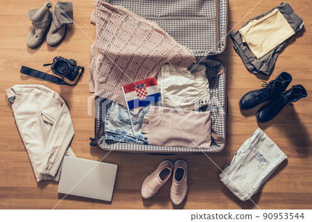 Woman's clothes, laptop, camera and flag of Croatia lying on the parquet floor near and in the open suitcase. Travel concept Woman's clothes, laptop, camera and flag of Croatia lying on the parquet floor near and in the open suitcase. Travel concept 90953544