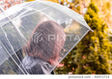 Autumn. Lonely sad redhead woman walking in a park, garden. View through wet transparent umbrella with rain drops. Rainy day landscape. Vintage Toned Autumn. Lonely sad redhead woman walking in a park, garden. View through wet transparent umbrella with rain drops. Rainy day landscape. Vintage Toned 90953714