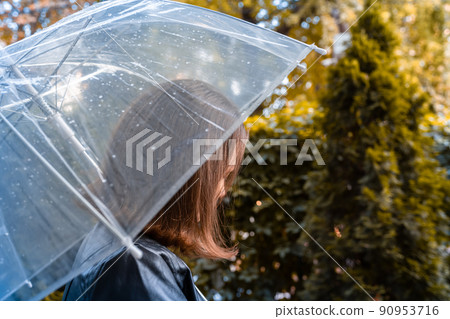Autumn. Lonely girl under a transparent umbrella with rain drops walking in a park, garden. Rainy day landscape Autumn. Lonely girl under a transparent umbrella with rain drops walking in a park, garden. Rainy day landscape 90953716