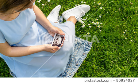 Ultrasound image pregnant baby photo. Woman holding ultrasound pregnancy picture on grass flower background. Pregnancy, medicine, pharmaceutics, health care and people concept. Ultrasound image pregnant baby photo. Woman holding ultrasound pregnancy picture on grass flower background. Pregnancy, medicine, pharmaceutics, health care and people concept. 90954057
