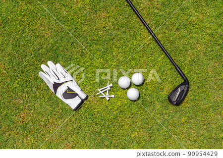 Top view of golf equipment on green grass on a golf course. Flat lay of golf club, balls, glove, tees Top view of golf equipment on green grass on a golf course. Flat lay of golf club, balls, glove, tees 90954429