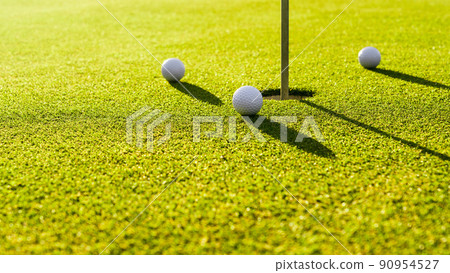 Three golf balls on the green grass near hole on a golf course at sunset 90954527