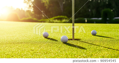 Three golf balls on the green grass near hole on a golf course at sunset 90954545