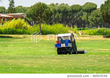 Golf course and golf cart collecting golf balls. Ballpicker on driving range of golf club Golf course and golf cart collecting golf balls. Ballpicker on driving range of golf club 90954548