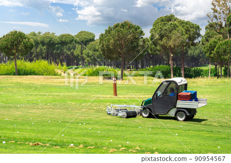 Golf course and golf cart collecting golf balls. Ballpicker on driving range of golf club Golf course and golf cart collecting golf balls. Ballpicker on driving range of golf club 90954567