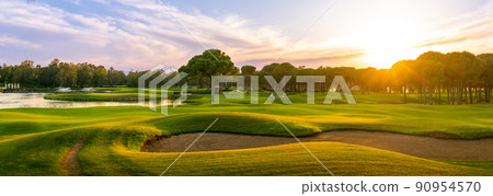 Golf course at sunset with beautiful sky and sand trap. Scenic panoramic view of golf fairway with bunker. Golf field with pines Golf course at sunset with beautiful sky and sand trap. Scenic panoramic view of golf fairway with bunker. Golf field with pines 90954570