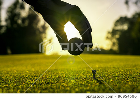 Golfer wearing glove placing golf ball on a tee at golf course 90954590