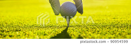 Closeup of golfer wearing glove placing golf ball on a tee at golf course Closeup of golfer wearing glove placing golf ball on a tee at golf course 90954599