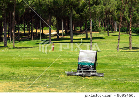 Golf course and golf cart collecting golf balls. Ballpicker on driving range of golf club Golf course and golf cart collecting golf balls. Ballpicker on driving range of golf club 90954603