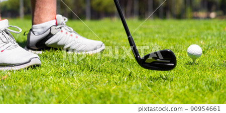 Man standing with golf iron club ready to hit a ball on green grass on golf course Man standing with golf iron club ready to hit a ball on green grass on golf course 90954661