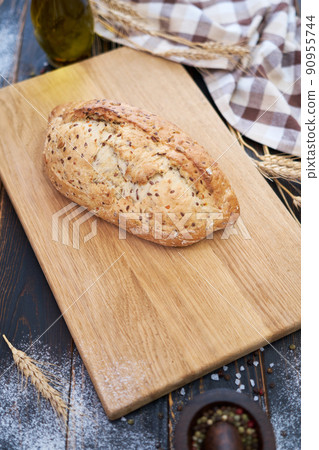 Fresh bread loaf on wooden cutting board at kitchen table Fresh bread loaf on wooden cutting board at kitchen table 90955744
