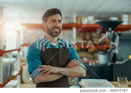 Smiling business owner standing on the background of own coffee roasting factory and looking away Smiling business owner standing on the background of own coffee roasting factory and looking away 90955767