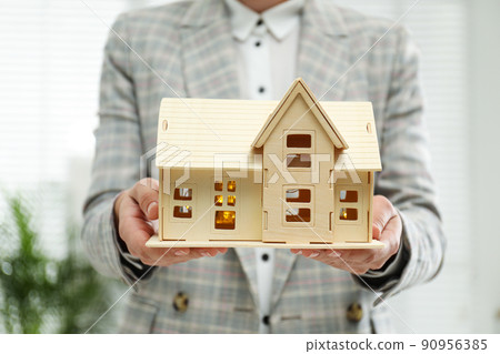 Real estate agent holding wooden house model with lights indoors, closeup Real estate agent holding wooden house model with lights indoors, closeup 90956385