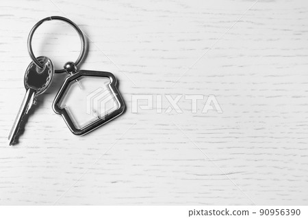 Key with trinket in shape of house on white wooden background, top view and space for text. Real estate agent services 90956390