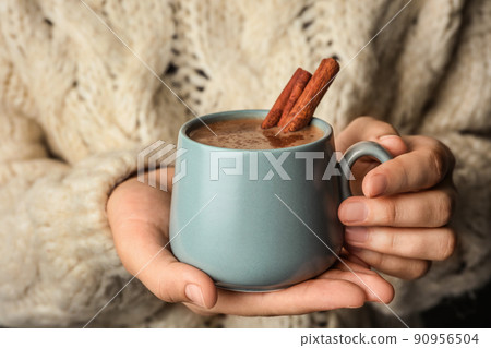Woman holding cup of delicious hot cocoa with cinnamon, closeup Woman holding cup of delicious hot cocoa with cinnamon, closeup 90956504